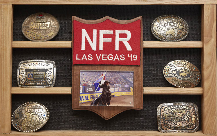 Shali lord’s buckle display with her NFR back number and a photo of her running barrels on her horse all hanging on the wall.